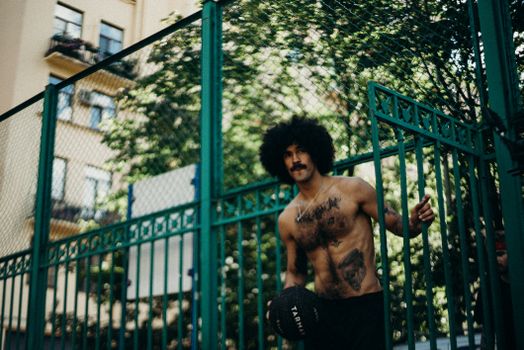 Tattooed man with afro hair holding a basketball in a street sportsground.