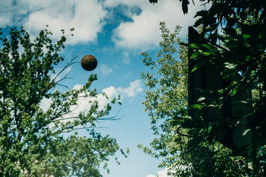A basketball hovers near the hoop with trees and blue sky in the background.