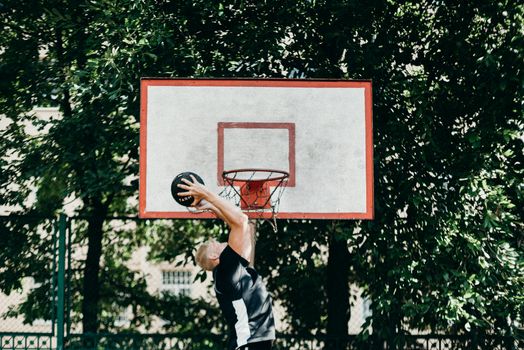 A man performing a slam dunk on an outdoor basketball court amidst lush greenery.
