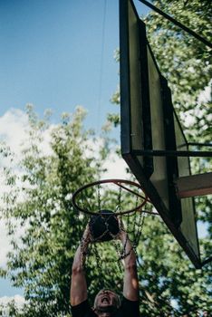A man performs a powerful basketball dunk outdoors, captured from a low angle against a clear sky.
