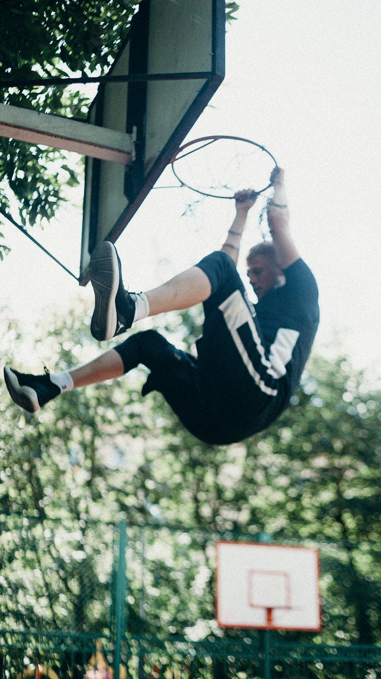 A Man Hanging On Basketball Hoop