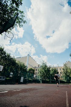 Basketball player practicing outdoors on a sunny day with a cityscape background.