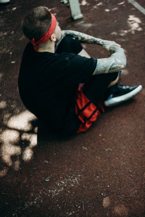 Free A tattooed man resting on an outdoor track wearing a headband and red shorts. Stock Photo
