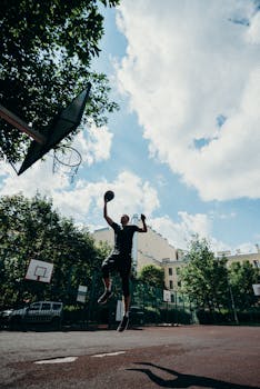 Action-packed shot of a man mid-air dunking a basketball on an outdoor court.
