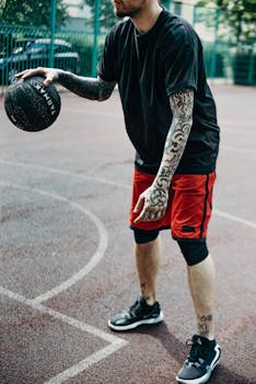 Tattooed man dribbles basketball on outdoor court, showcasing fitness and sport.