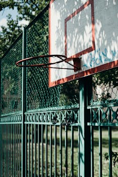 Close-up of an outdoor basketball hoop on a sunny day with a green fence background.