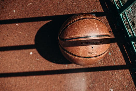 Detailed view of a basketball resting on a sunlit outdoor court with shadows.