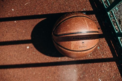 Free Detailed view of a basketball resting on a sunlit outdoor court with shadows. Stock Photo