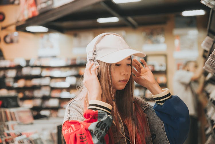 Trendy Asian Student In Headset And Cap In Book Shop