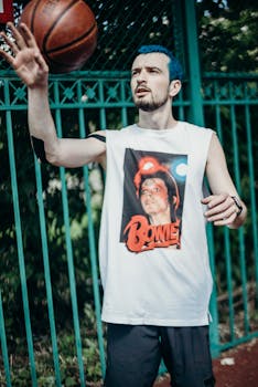 A man with blue hair playing basketball outdoors, wearing a Bowie t-shirt.