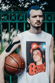 Stylish man with blue hair holding a basketball, wearing a Bowie tank top.