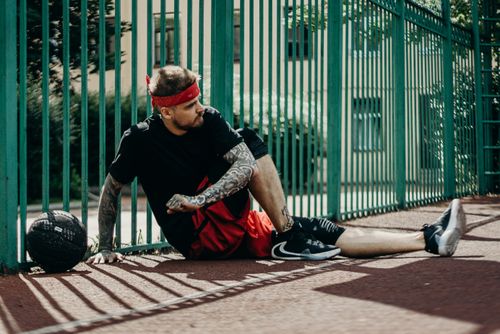 Free Tattooed basketball player resting on the court beside a green fence. Stock Photo