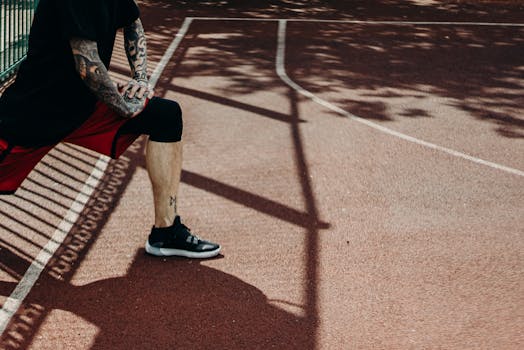Tattooed man stretches on a sunny outdoor basketball court, focusing on fitness.