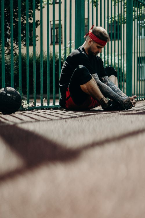 Free Tattooed man in sportswear resting outdoors by a fence on a sunny day. Stock Photo
