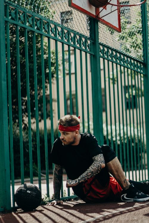 Free Tattooed man in sportswear sits on a basketball court, showcasing a sporty lifestyle. Stock Photo