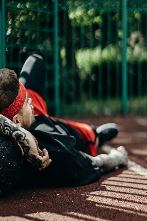 Free A man with tattoos and a red headband lying on the ground of a sports field, relaxing. Stock Photo