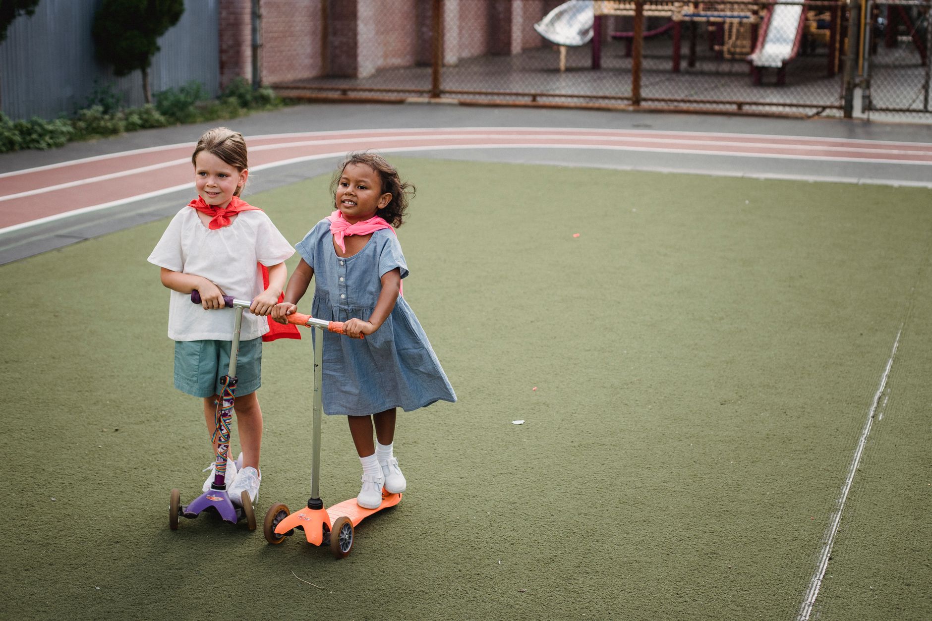 Two children enjoying a day outdoors, riding scooters on a playground.