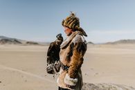 Mongolian man standing with eagle on hand in spacious valley