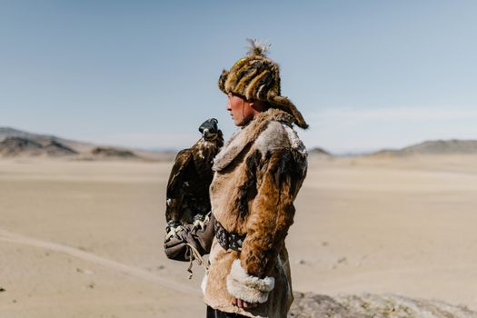 Mongolian man standing with eagle on hand in spacious valley