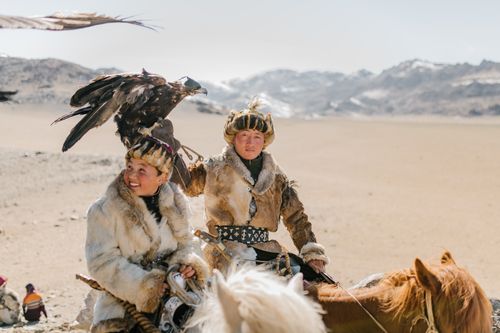 Free Young Mongolian hunters wearing local warm clothes carrying golden eagles on hands and riding horses along spacious rough highland on winter weather Stock Photo