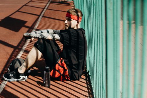 Free Tattooed man in sportswear takes a break on outdoor basketball court, midday sunlight. Stock Photo