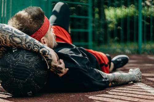 Free Man in Black and Red Jacket Lying on Brown Wooden Bench Stock Photo
