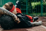 Man in Black and Red Jacket Lying on Brown Wooden Bench