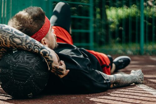 Free Tattooed man relaxes on basketball court with a ball, displaying athletic lifestyle. Stock Photo