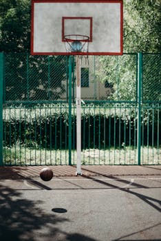 An outdoor basketball hoop with a ball on a sunny day.