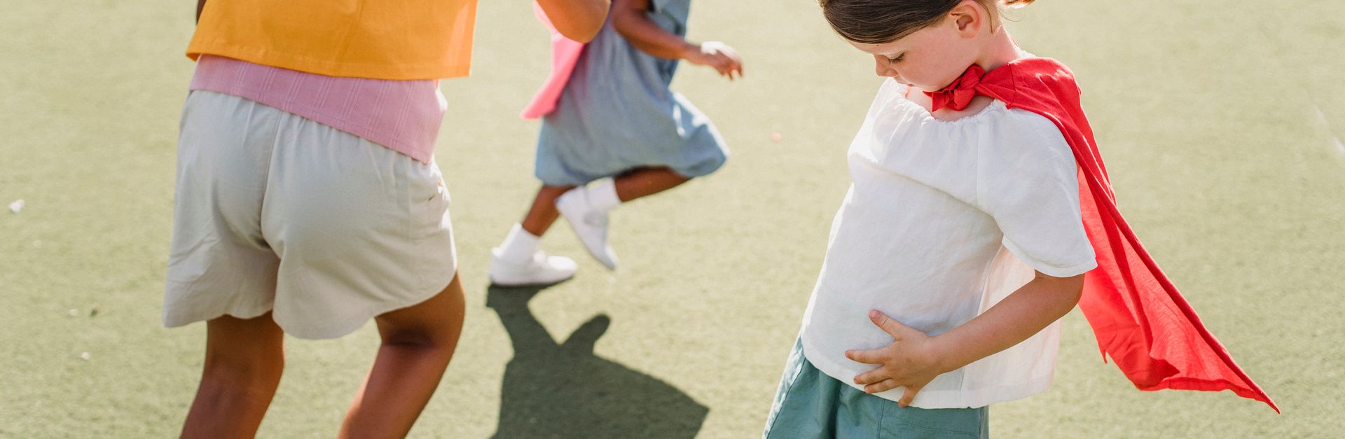 Children dressed as superheroes playing and running outdoors on a sunny day.