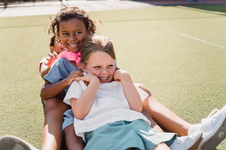 Kids Sitting Behind Each Other On Grass And Laughing 