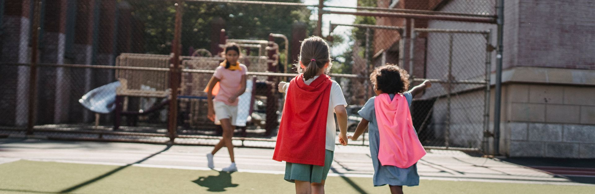 Kids enjoying outdoor playtime at a playground, wearing capes and running freely.