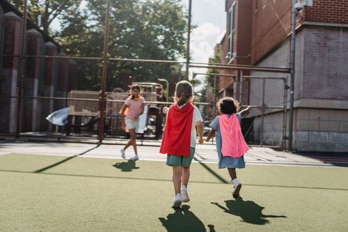 Free Kids enjoying outdoor playtime at a playground, wearing capes and running freely. Stock Photo