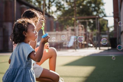 Free Two children enjoy blowing bubbles outdoors on a sunny day, capturing the essence of carefree childhood. Stock Photo