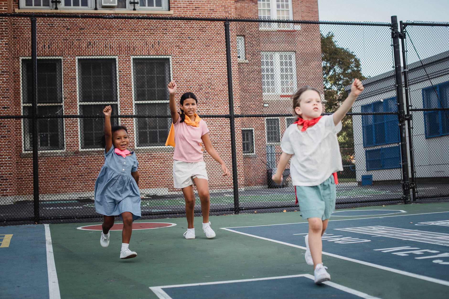 IB school sports day Egypt — Children role-playing as superheroes during outdoor playtime at a school's basketball court.