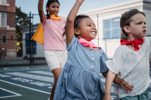 Three kids enjoying superhero play on a sunny outdoor court.