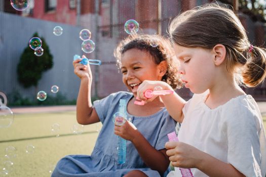 Two happy children playing with soap bubbles outdoors on a sunny day, smiling and having fun.