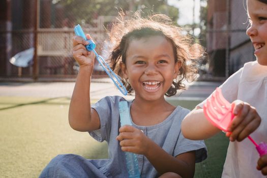 Two happy children enjoying blowing bubbles outside on a sunny day, sharing fun and laughter.