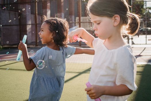 Two young girls enjoy playing with soap bubbles in a sunny outdoor setting, capturing joy and leisure.