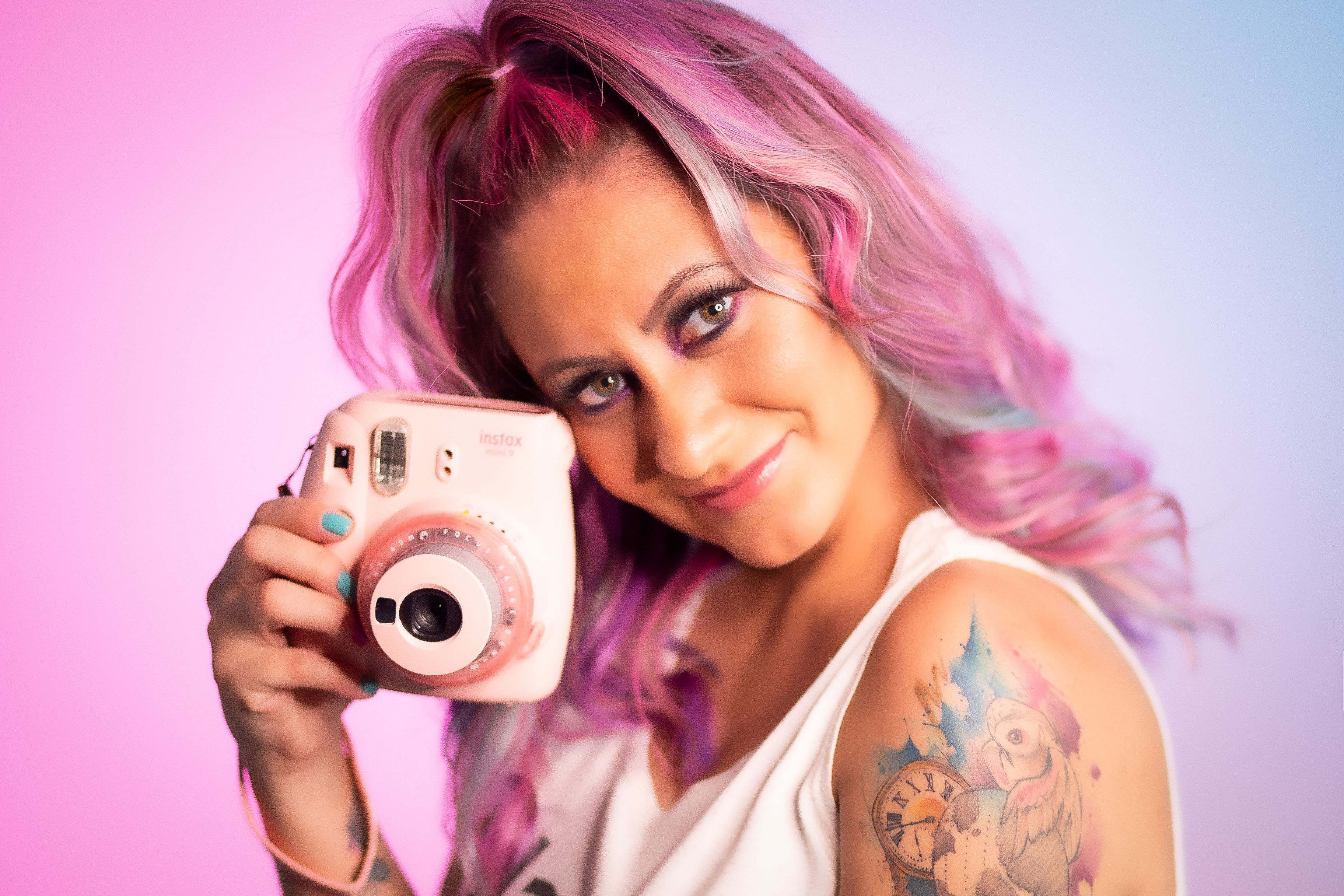Stylish woman with pink hair holding an Instax camera, showcasing colorful tattoo.