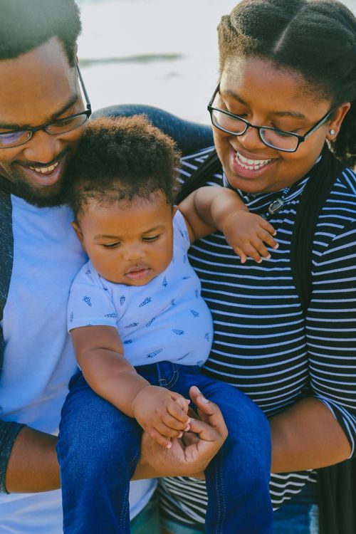 Free A joyful family portrait with parents holding their baby in a sunny outdoor setting. Stock Photo