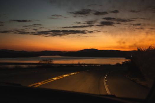 A scenic drive at sunset with silhouetted mountains and a winding road, capturing a moody sky.