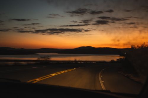 Free A scenic drive at sunset with silhouetted mountains and a winding road, capturing a moody sky. Stock Photo