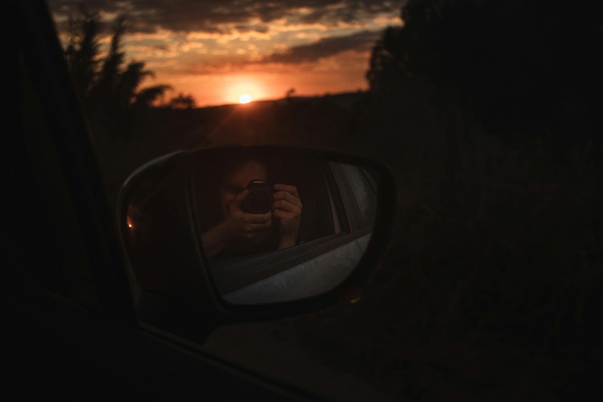 A mesmerizing sunset captured in a car side mirror with a camera reflection.