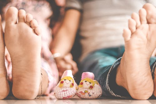 Free Ground level barefoot kids in casual clothes sitting on floor together near handmade small toys and holding hands Stock Photo