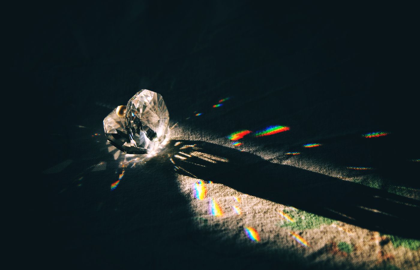 A diamond-shaped crystal casting rainbow reflections on a surface with dramatic lighting.