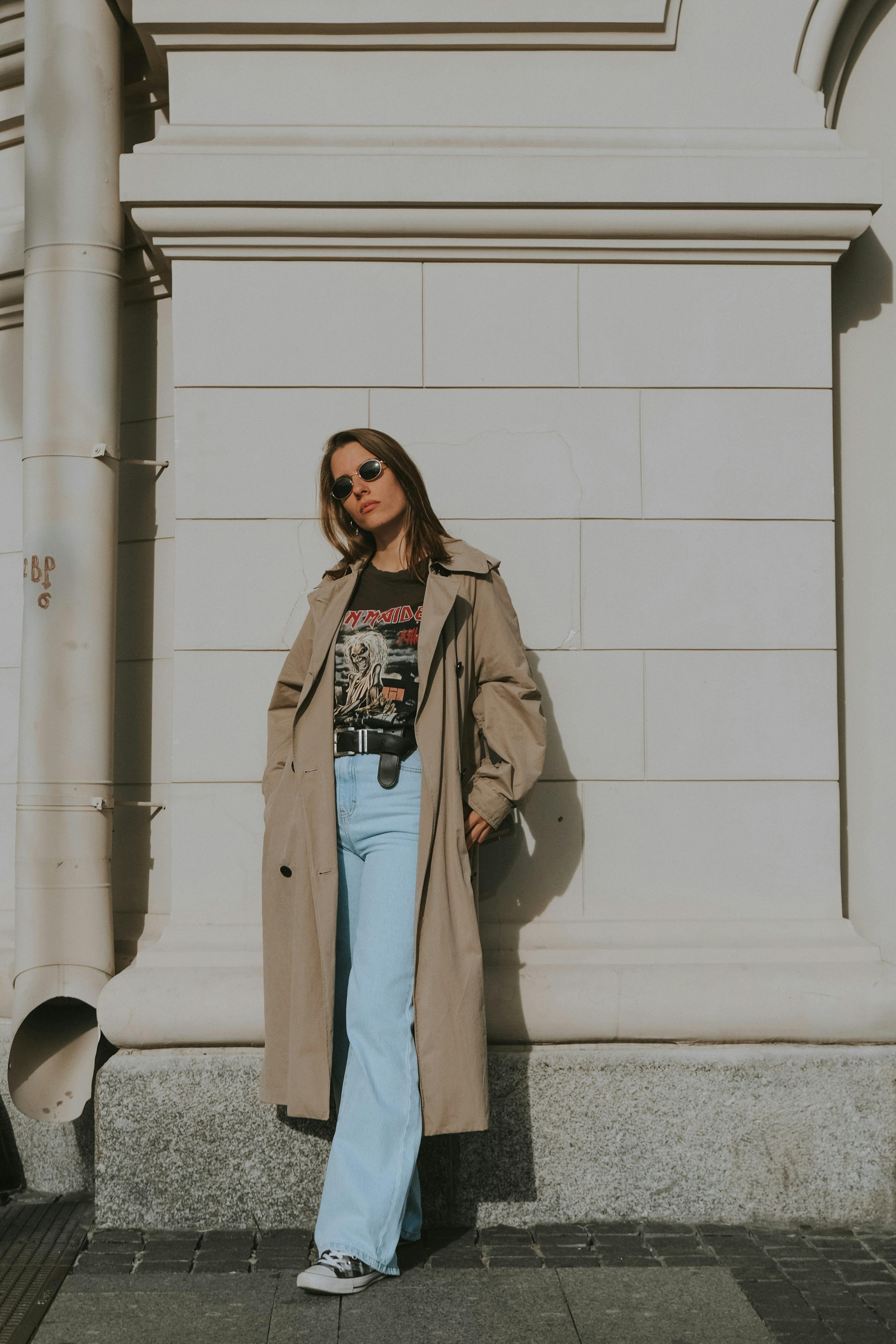 Full body of young female in stylish clothes and sunglasses standing on pavement near building at daytime