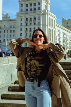 Stylish female in trendy clothes standing on stone stairs and smiling while looking at camera