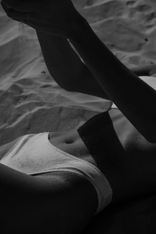 Free Black and white of faceless slim female in bikini lying on sandy beach at daylight Stock Photo