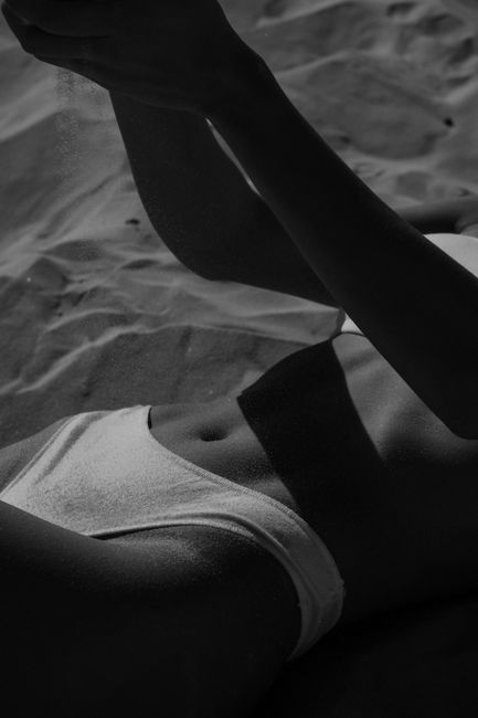 Black and white of faceless slim female in bikini lying on sandy beach at daylight